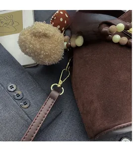 Détail d'un sac seau en daim marron avec boule en peluche et attache de sangle perlée