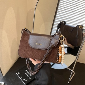 Detail van donkerbruine crossbodytas met mat leren stiksel en een houten kralenhanger