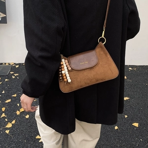 Detail van bruine suède schoudertas met leren flap en houten kralenhanger op een model