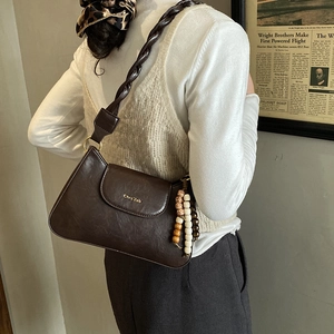 Detail van bruine lederen tas met gevlochten riem en vintage houten kralen hangers