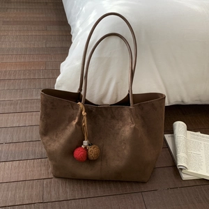 Detail of dark brown suede tote bag with plush charm on warm wooden background