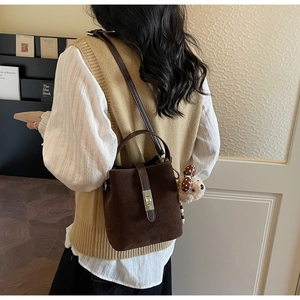 Détail d'un sac seau marron givré avec pendentif ours porté par un mannequin en intérieur