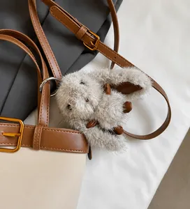 Détail d'un charm de sac lapin en peluche beige avec anneau sur une bandoulière en cuir