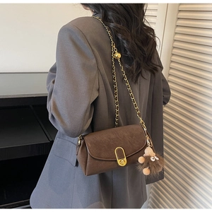 Détail d'un sac bandoulière en cuir marron avec chaîne dorée et breloque peluche monstre