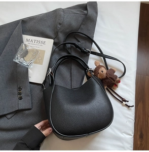 Detail of black lychee grain leather bucket bag with cute teddy bear charm accessory