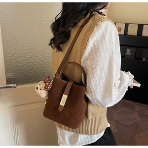 Détail du sac seau en daim marron foncé avec fermoir doré et breloque ours en peluche