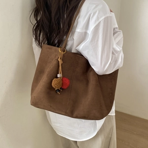Close-up of caramel brown suede tote bag with decorative plush charms and gold hardware