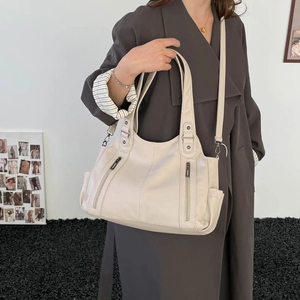 Detail view of cream-colored hobo bag featuring vertical zipper pockets and soft leather texture