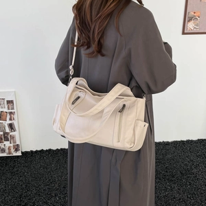 Detail of cream white tote bag featuring pebble leather texture and metal zipper pockets