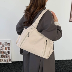 Detailed macro view of the cream leather tote bag with vertical zipper pockets and rivets