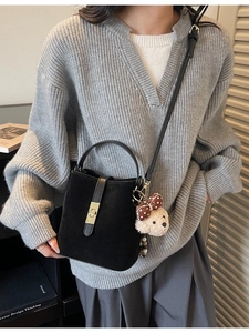 Sac seau noir mat minimaliste avec fermoir doré et charme d'ours sur un pull gris chic