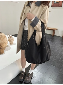 Detail of a large black nylon tote bag with silver grommets worn by a model in a trench coat