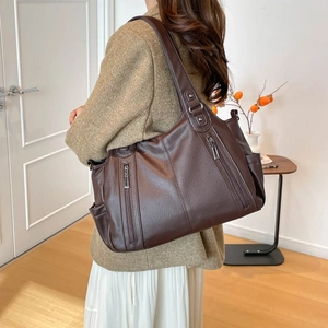 Detail of the large brown leather tote bag showing side zippers and functional pockets