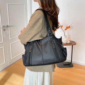 Close-up of black lychee-textured leather tote bag with multiple zipper pockets worn by model