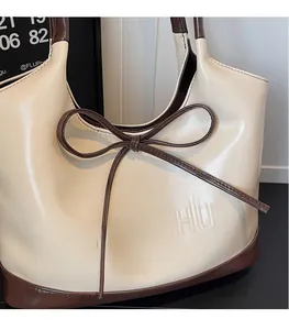 Detailweergave van de crème leren shopper met bruine strik en GONGZHU reliëflogo