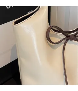 Detail van gebroken witte leren draagtas met GONG-logo in reliëf en strikdecoratie