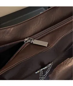 Dettaglio della cerniera metallica e della catena decorativa sulla borsa in pelle marrone
