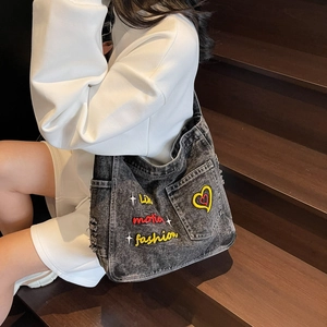Denim tote bag with colorful embroidery and distressed details shown on a model