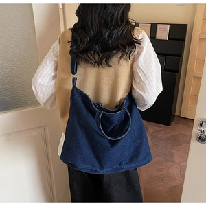 Detail view of large denim tote bag worn as a shoulder bag showing the dark blue texture