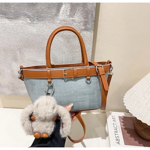 Détail d'un sac seau bleu tissé avec poignées en cuir marron et pendentif lapin en peluche