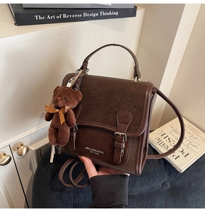 Detail of dark brown vintage faux leather handbag with a plush bear charm and metal buckles