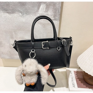 Détail d'un cabas noir tissé avec boucle décorative et breloque lapin en peluche
