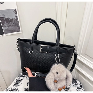 Détail d'un sac à main noir texturé avec boucle argentée et breloque lapin en peluche
