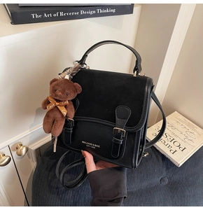 Detail view of black handbag featuring matte texture flap and cute bear pendant with ribbon