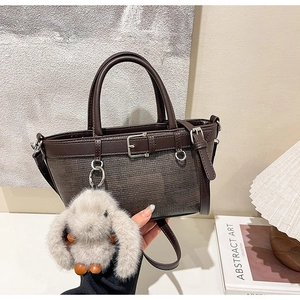 Détail d'un sac à main tissé avec poignées en cuir marron et breloque lapin en peluche