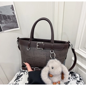 Gros plan du sac à main marron foncé texturé avec bordure en cuir et breloque lapin en peluche