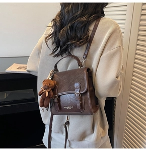 Detail of a brown vintage leather backpack with golden logo and teddy bear charm