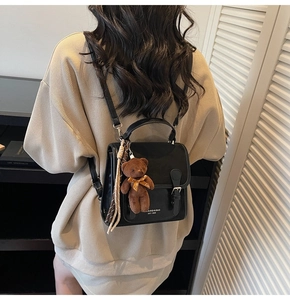 Detail view of black vintage school style backpack with metal buckle and bear pendant