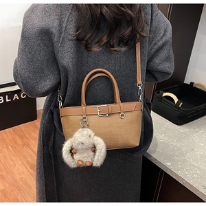 Détail d'un sac seau tissé marron avec garniture en cuir et breloque lapin en peluche