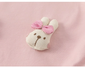 Close-up of cute cream bunny patch with pink silk bow on soft knitted fabric background