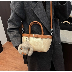 Détail du sac seau tissé beige avec poignées en cuir marron et breloque lapin en peluche