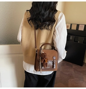 Close-up of vintage brown crossbody bag with plush bear charm and striped scarf detail