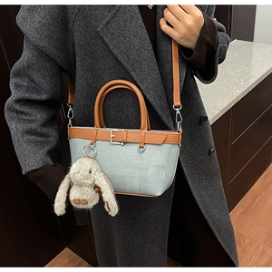 Détail d'un sac à main gris-bleu texturé avec poignées en cuir marron et breloque lapin