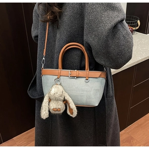 Détail d'un sac seau gris tissé avec poignées en cuir marron et un charmant lapin en peluche