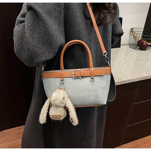 Détail du sac seau en toile grise avec bordure en cuir marron et pendentif lapin en peluche