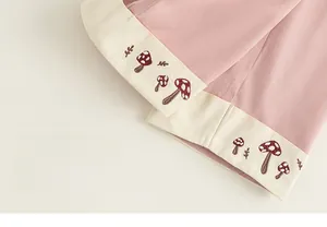 Dettaglio dei pantaloni rosa per bambina con orlo patchwork beige e ricamo a fungo