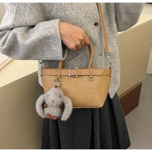 Détail du sac bandoulière kaki avec texture tissée, poignée en cuir et breloque lapin