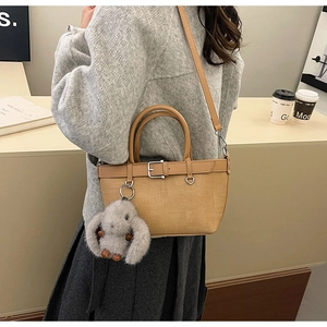Détail du sac seau tissé avec poignées en cuir et accessoire de charme lapin en peluche