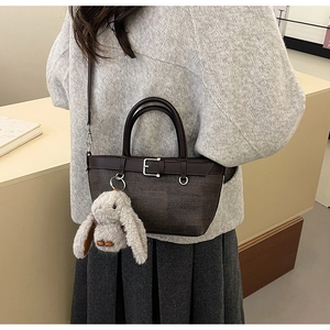 Détail d'un sac seau marron foncé texturé avec un joli charme de lapin en peluche et boucle
