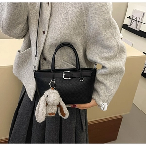 Détail du sac seau noir tressé avec boucle métallique et pendentif lapin élégant