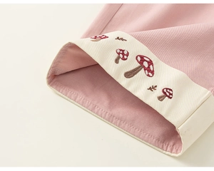 Dettaglio dei pantaloni in cotone rosa con ricami di funghi e orlo risvoltato