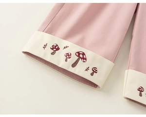 Dettaglio dei pantaloni in cotone rosa con ricamo a fungo e risvolto beige ai piedi