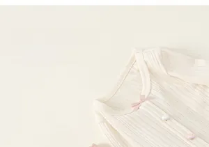 Detail of off-white rib knit top with pink bow and buttons for baby girls