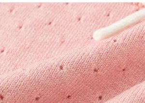 Dettaglio di morbida maglia rosa con trama traforata e cordoncino in cotone bianco