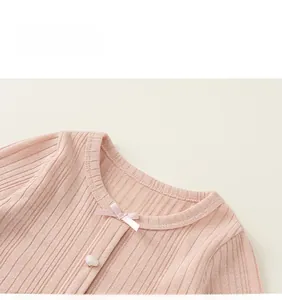 Close-up of pink knit girl cardigan with heart pearl button and a delicate bow detail