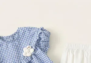 Detail view of blue plaid cotton blouse with 3D flower applique and white summer shorts